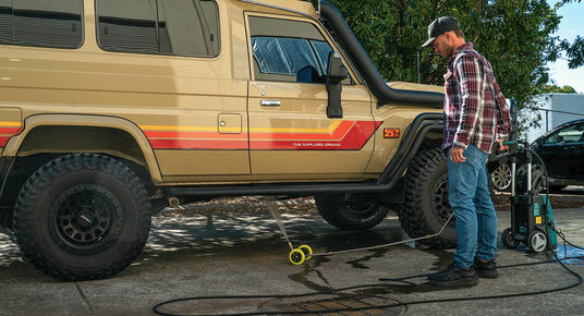 Person using a pressure washer on a beige SUV with red stripes