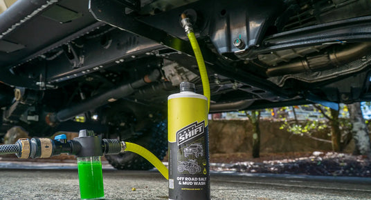 Car undercarriage with a yellow bottle labeled 'Shift' and green liquid being added.