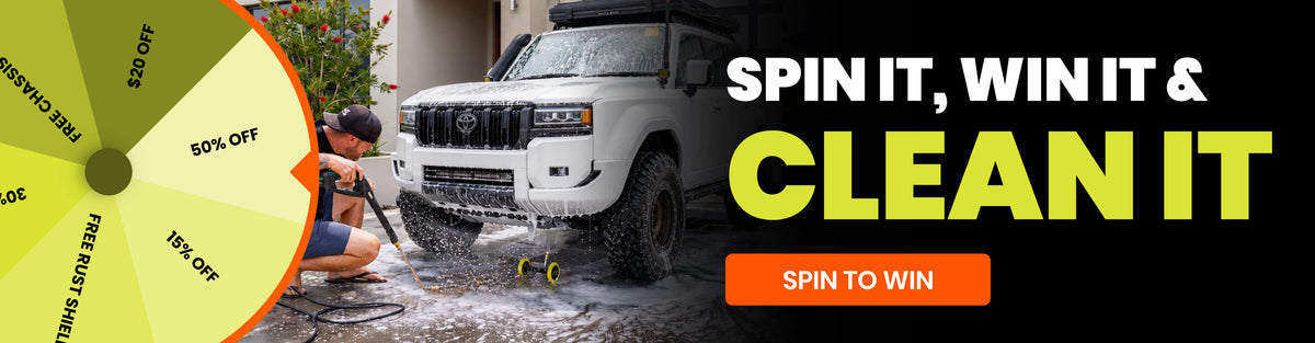 Promotional banner for a car wash service featuring a white SUV being washed, a yellow discount wheel on the left, and large text reading 'SPIN IT, WIN IT & CLEAN IT' with an orange 'SPIN TO WIN' button.
