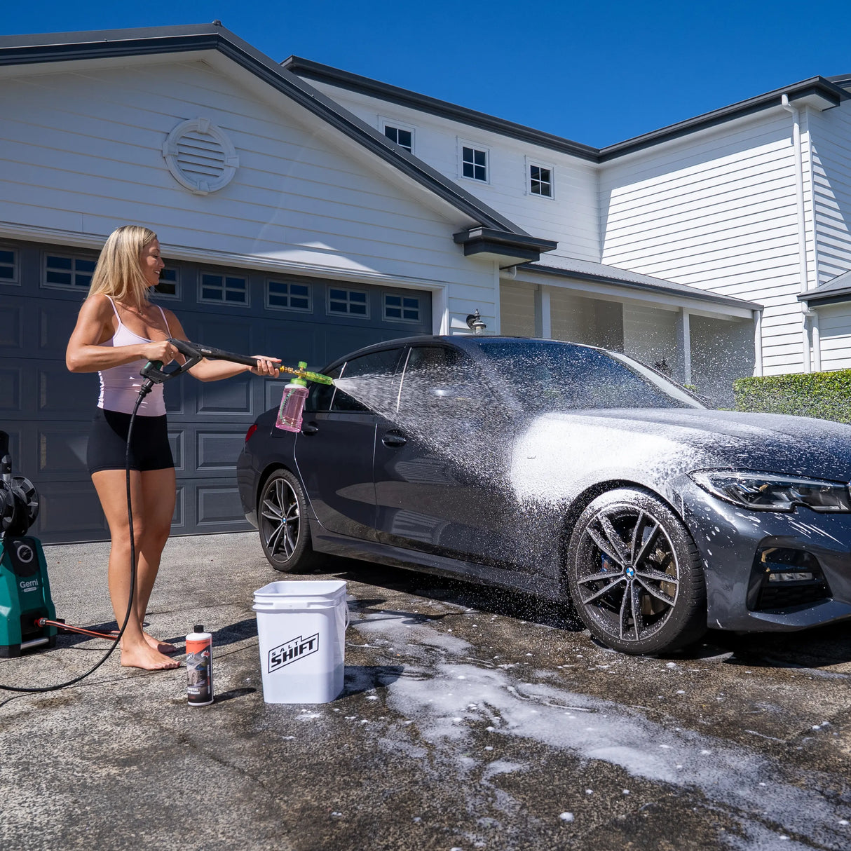Woman washing a car with a pressure washer in front of a house
