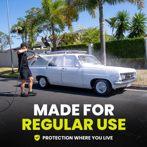 Person washing a white vintage car with palm trees and a clear blue sky in the background.