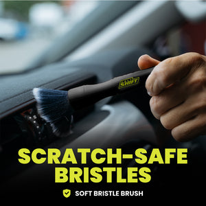 Hand using a soft bristle brush to clean car interior with 'Shift' branding, text 'Scratch-Safe Bristles' displayed.