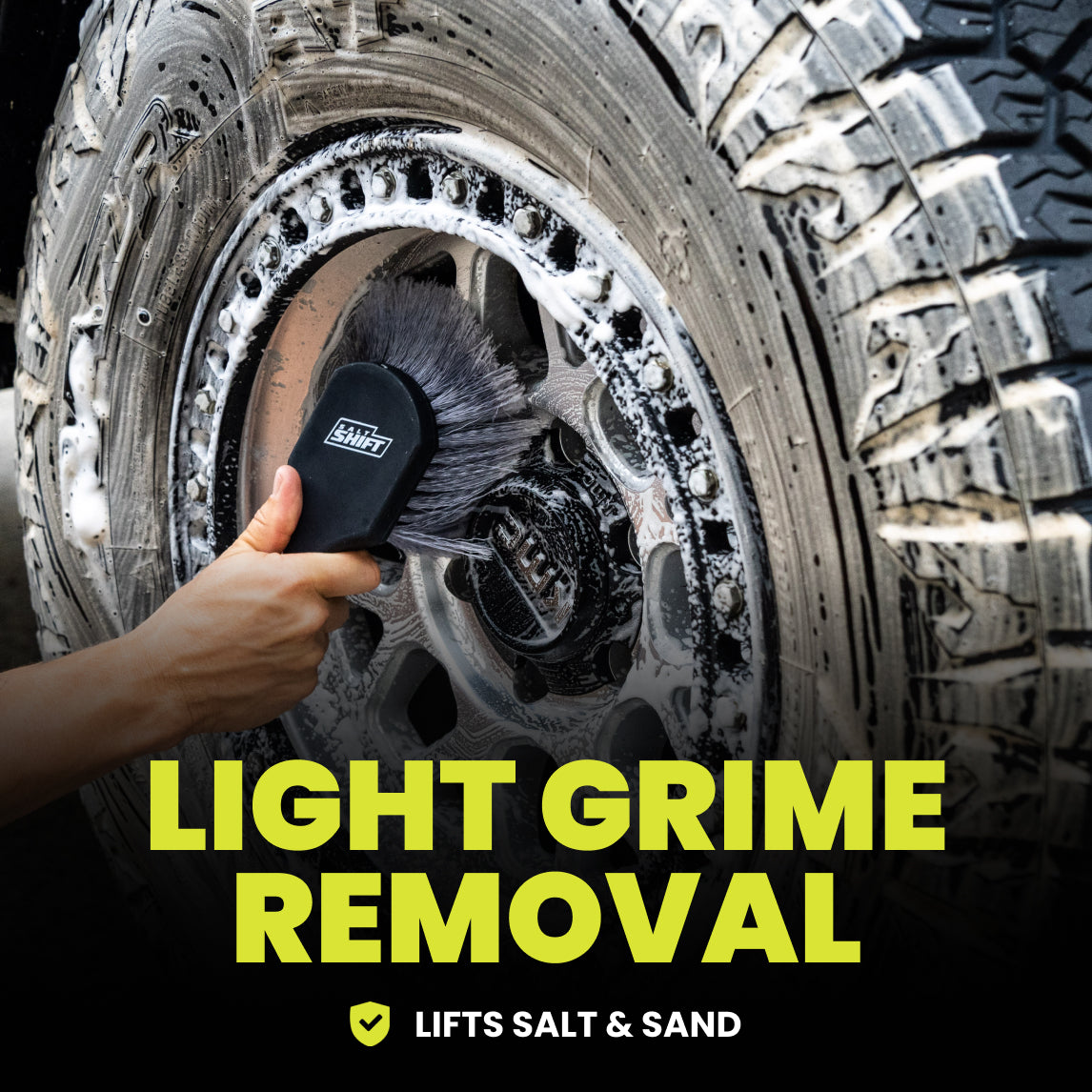 Person cleaning a tire with a soft brush against a dark background.