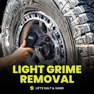 Person cleaning a tire with a soft brush against a dark background.