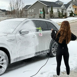 Person washing a snow-covered car with a pressure washer in a residential area.