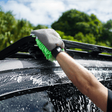 A hand using the Salt Shift 2-in-1 Wash Mitt to clean the top of a soapy vehicle. The mitt's dual-sided design is visible with the green microfiber strands in action.