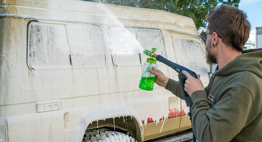 Person washing a van with a pressure washer and bottle of cleaning solution.