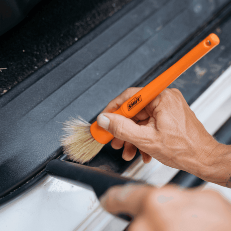 A person uses a Salt Shift detailing brush to clean a car.