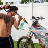 Man using a Salt Shift pump action foamer to clean a dirt bike wheel, removing mud and grime for off-road maintenance.