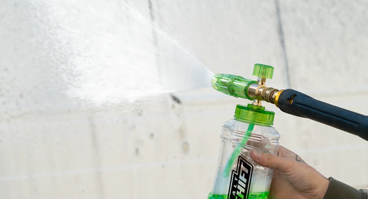 Person holding a bottle with a green spray nozzle against a white background