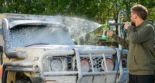 Person washing a large vehicle with a hose outdoors
