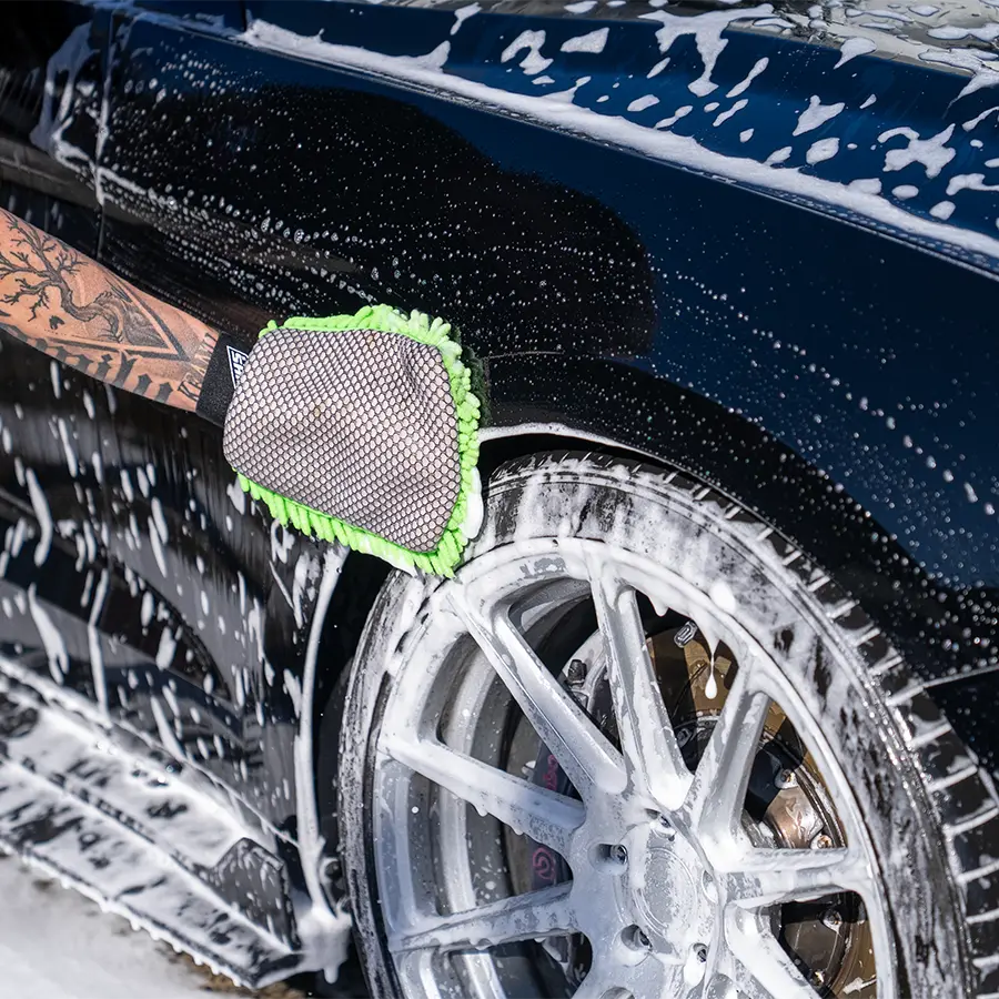 Person washing a car with a green sponge on a soapy wheel