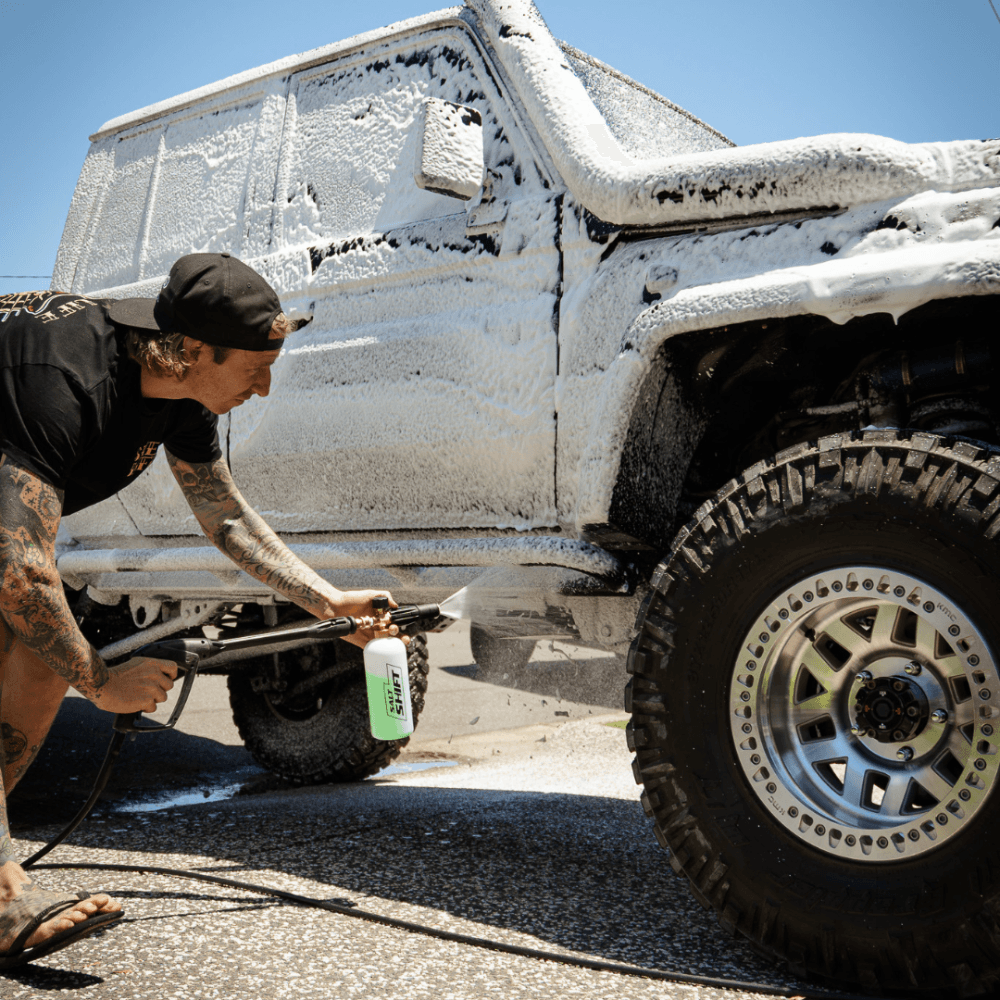 A person uses a Salt Shift foam cannon to spray a truck with thick cleaning foam.