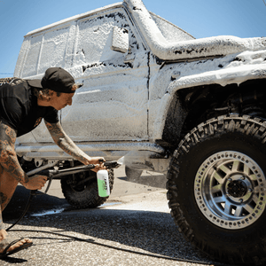 A person uses a Salt Shift foam cannon to spray a truck with thick cleaning foam.