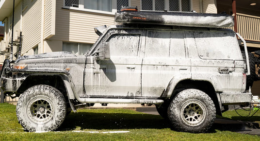 Silver off-road vehicle with a roof rack parked on grass in front of a house.