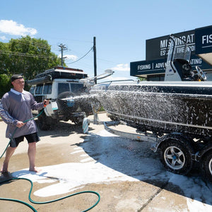 A person uses a Salt Shift foam cannon to spray a boat with cleaning foam.