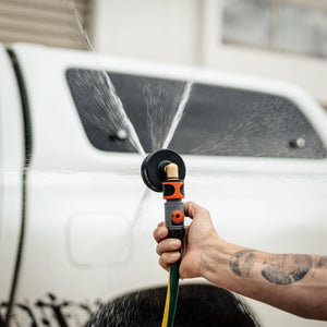 A person holds a Salt Shift chassis flusher spraying water in multiple directions with a truck on the background.