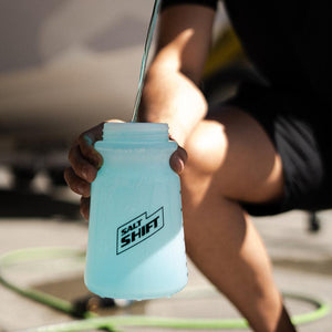 A person pours liquid into a Salt Shift foam cannon bottle, preparing for a wash.