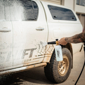 A person uses a Salt Shift foam cannon to spray a truck with thick cleaning foam.