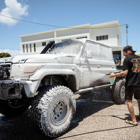 A person uses a Salt Shift foam cannon to spray a truck with cleaning foam.