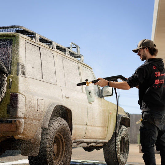 A person uses a Salt Shift foam cannon to spray a truck with thick cleaning foam.