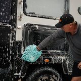 Man washing a 4WD caravan with a microfibre mitt and foaming cleaner, removing dirt and grime for a spotless finish.