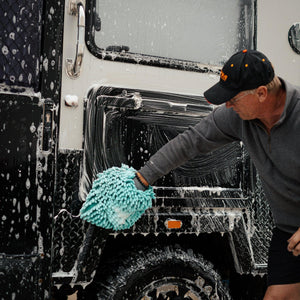 Man washing a 4WD caravan with a microfibre mitt and foaming cleaner, removing dirt and grime for a spotless finish.
