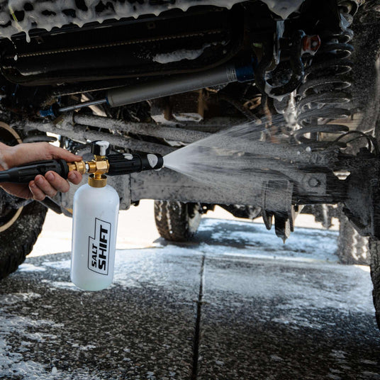 A person uses a Salt Shift foam cannon to spray a 4x4 undercarriage with cleaning foam.