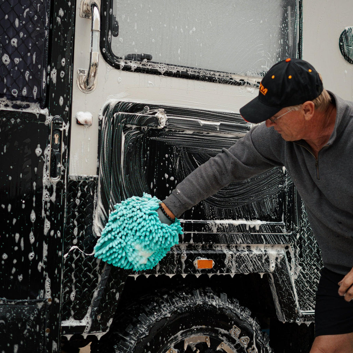 Man washing a 4WD caravan with a microfibre mitt and foaming cleaner, removing dirt and grime for a spotless finish.