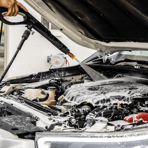 A person pressure washes a foamed engine bay for a deep clean.